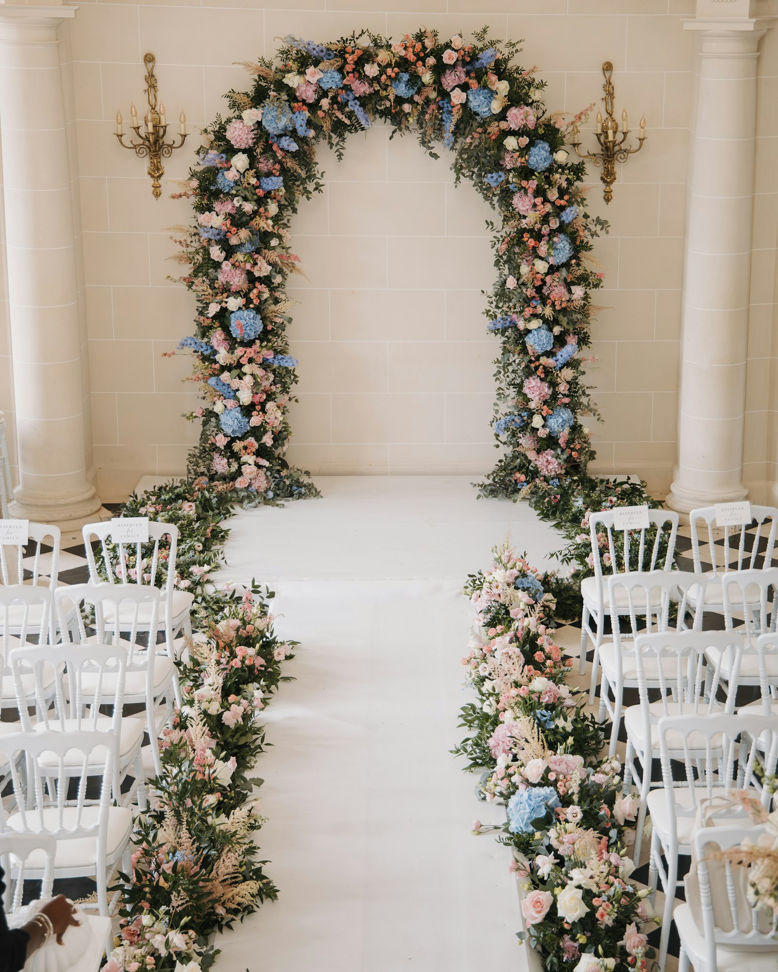 Rows of chairs set out for an outdoor wedding ceremony beneath a floral archway